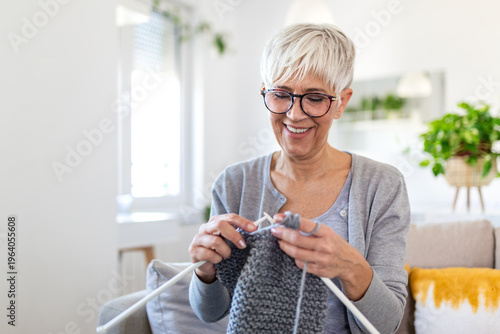 Billede på lærred Senior woman knitting grey wool sweater on sofa at home