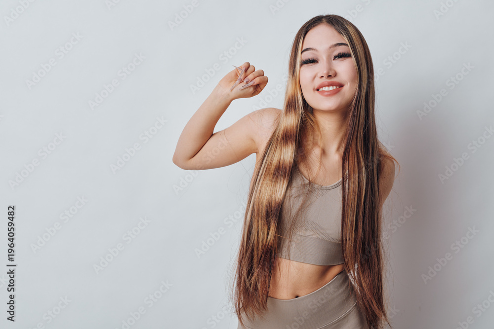 Fototapeta premium Young woman with long hair wearing a crop top and skirt standing against white background. Smiling female posing with raised arm and relaxed expression in studio setting.