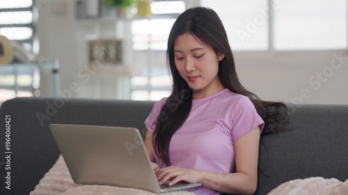 Asian adult woman works from home using laptop computer for remote study at comfortable living room