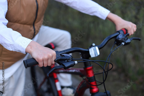 Close up of a boys hands gripping the handlebars of a red bike, brake levers, gear shifter, and reflector visible, poised for a ride in soft outdoor light.