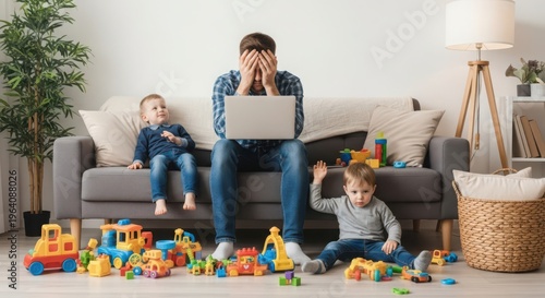 Overwhelmed father with laptop sits on couch surrounded by playing children and toys in messy living room
