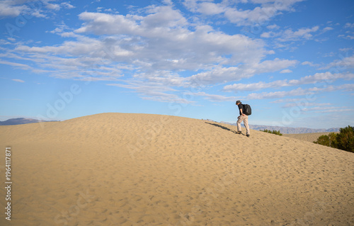 Man walking uphill on sand dunes. Mesquite Flat Sand Dunes. Death Valley National Park. USA.