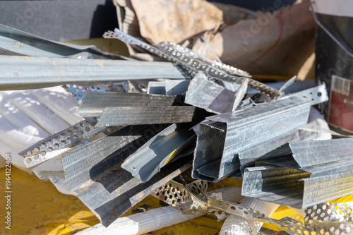 Pile of galvanized steel profiles and metal scraps from construction site renovation, industrial waste and building materials close-up.