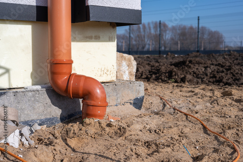 PVC rainwater downspout connected to underground drainage pipe at house foundation, stormwater drainage installation during residential construction.