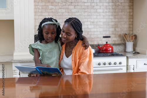 African American mother and child in green dress sitting at kitchen counter reading blue book