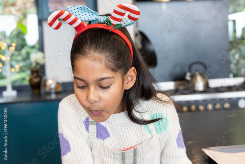 Indian child girl at kitchen counter leaning pursing lips cooling food kettle apron headband lights