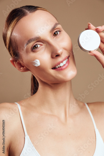 Tableau sur toile Young woman applying cream on face smiling looking at camera natural skincare ro