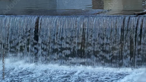 Soft water cascades over smooth rocks, creating calming sound and sparkling reflections. The early morning light brings tranquil atmosphere, perfect for relaxation and reflection.