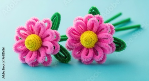 A pair of lively pink flowers created with pipe cleaners rests on a blue surface. The elaborate design emphasizes the ingenuity and craftsmanship in this one of a kind decor.