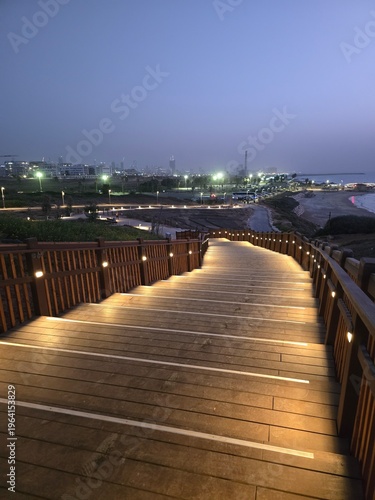 Illuminated curved wooden boardwalk at dusk by urban waterfront