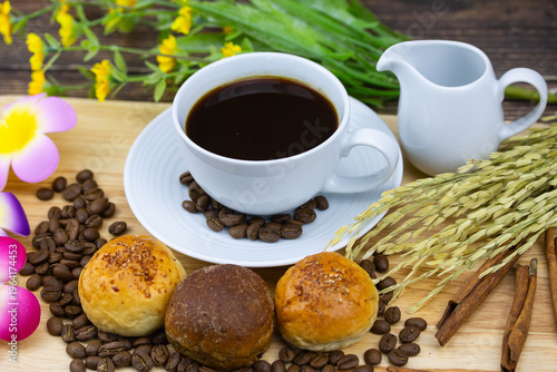 Still life coffee scene with cup of black coffee, bread, coffee beans, sunflower and cinnamon on wooden background, warm cozy cafe