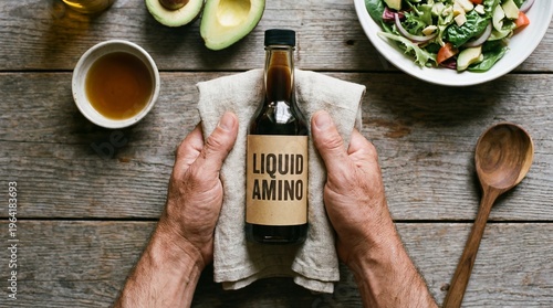 High Angle Flat Lay of Hands Holding a Bottle of Liquid Amino Acids Seasoning with Health Food and Fresh Salad on a Rustic Wooden Table