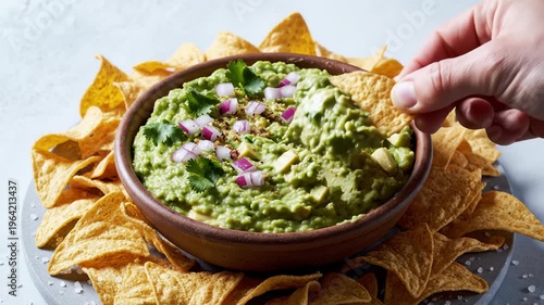 Hand Dipping Tortilla Chip Into Fresh Guacamole Surrounded by Chips