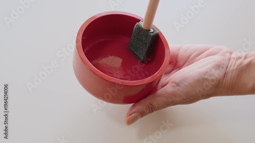 Hand Holding Red Bowl While Applying Paint With Foam Brush in Closeup Crafting Scene