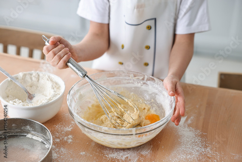Child mixing dough in bowl at wooden table indoors, closeup