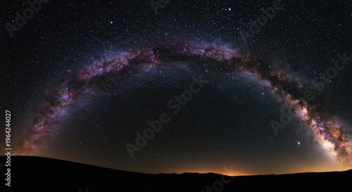 Brilliant arc of the galaxy stretches across a dark, starry night sky above a silhouetted horizon