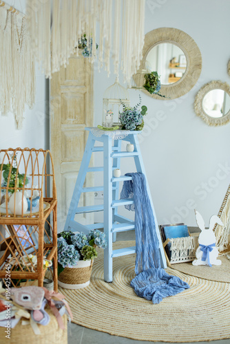 Elegant light blue Easter decor in a bright nursery with a wooden ladder, birdcage, bunny figures, and hydrangeas in a minimalist Scandinavian interior.