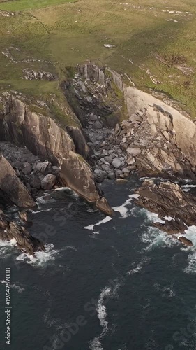 Jagged rock formations and grassy slopes overlook the churning ocean waves.