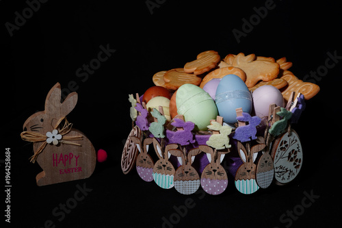Easter still life featuring a purple felt basket decorated with wooden bunny clothespins, filled with colorful eggs and a white plush rabbit.