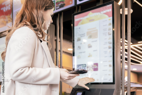 Εκτύπωση καμβά Woman selecting food on touchscreen kiosk in modern restaurant environment with