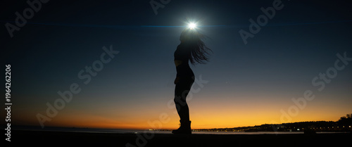 Woman silhouette standing at sunset hour by the ocean