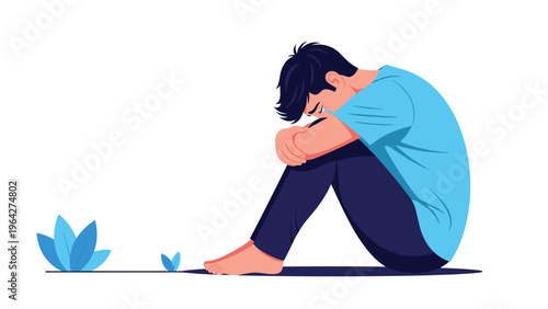 Sad and lonely young boy sits on the ground with his head down on his knees expressing feelings of depression or isolation.