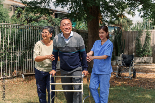 Elderly men and women happily exercise under a big tree. Elderly man holding a walker