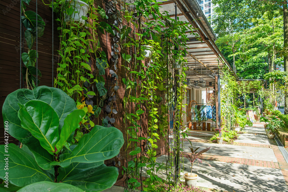 Obraz premium Outdoor cafe in Kuala Lumpur, Malaysia with lush greenery, hanging plants and shaded seating area. Urban lifestyle, street restaurant, eco design and sustainable architecture integrated in modern city