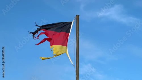 wind-torn and frayed Tattered German Flag in Wind flies from a flagpole against a bright blue sky, evoking themes of resilience, crisis, or political commentary