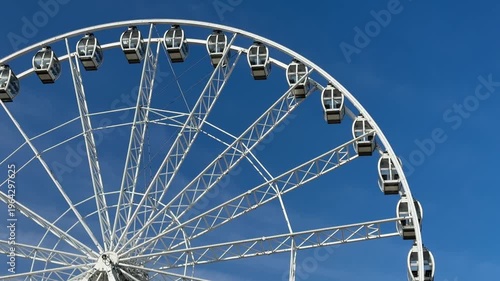 Low-angle view of a large, white modern Ferris wheel with glass gondolas against a deep blue, cloudless sky