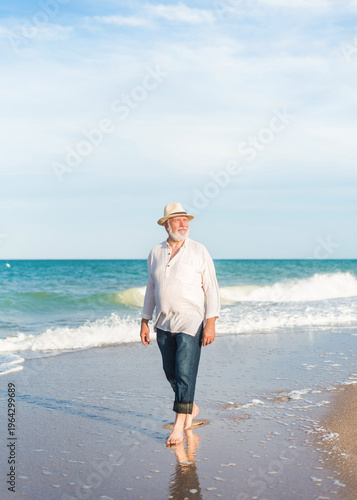 Photos Senior man walking barefoot along shoreline enjoying peaceful summer beach vacat