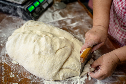 Baker prepares dough on wooden table in kitchen during morning hours for fresh bread making