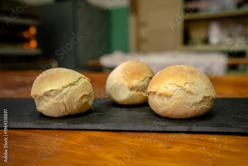 Foto Freshly baked bread rolls on a black tray in a bakery during the afternoon