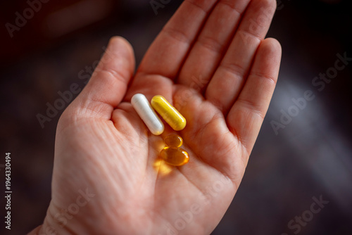 Close-up of a woman's hand holding three different supplement capsules in her palm, white, yellow, and clear gel pills, healthy lifestyle and vitamin concept