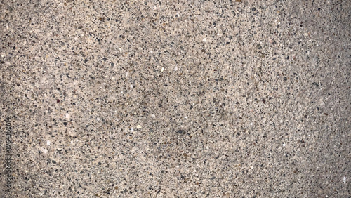 A rough, speckled concrete surface texture in close-up, showcasing embedded small aggregate stones in mixed grey and brown tones, perfect for versatile material backgrounds.