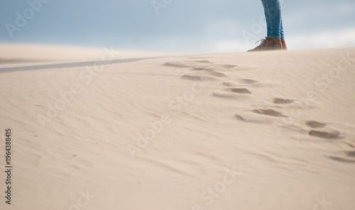 Tableau sur toile Windblown sand dune with footprints and walking traveler in coastal desert landscape