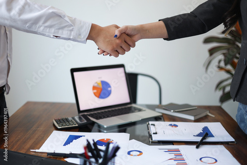 Schilderij op canvas Businesspeople shaking hands in the meeting over a desk with business documents and laptop for the start or culmination of a professional relationship or negotiation