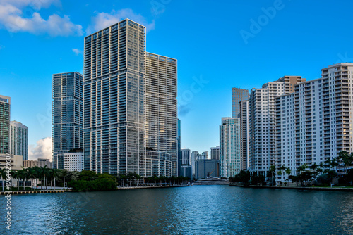 Modern luxury high-rise residential apartment buildings lining the banks of a river under a clear blue sky in Miami Florida.