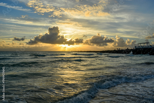 Dramatic golden sunset over the ocean with white waves crashing on the shore and sun rays breaking through the clouds.