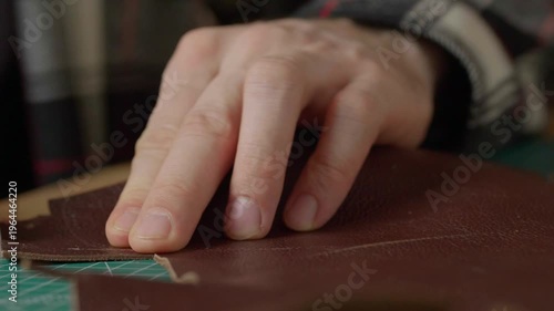 Close-up of a hand with a sharp leather cutting knife trimming or cutting a piece of natural brown leather. Fabrication technique.