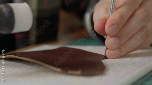 A hand holds a hammer and punch, making even angles in a piece of leather.
