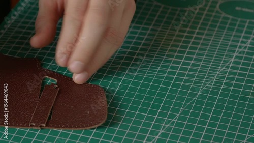 Close-up of a hand with a sharp leather cutting knife trimming or cutting a piece of natural brown leather. Fabrication technique.