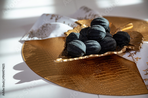 Black nut-shaped cookies with filling on a golden leaf-shaped plate on a table in the rays of the sun
