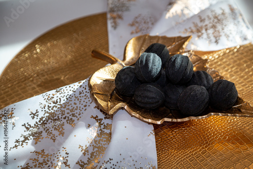 Black nut-shaped cookies with filling on a golden leaf-shaped plate on a table in the rays of the sun