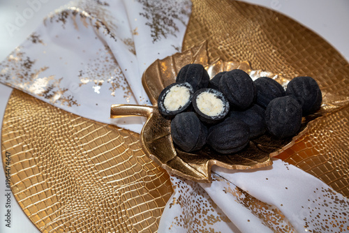 Black nut-shaped cookies with filling on a golden leaf-shaped plate on a table in the rays of the sun