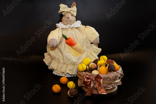 A full basket of multi-colored baked nuts against the backdrop of a bunny with a carrot in a beautiful dress on a black background