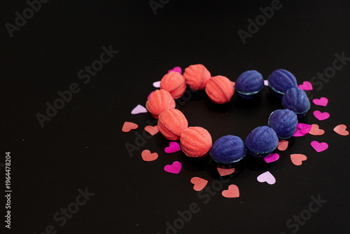Heart shape made from baked nuts with filling on a black background with multi-colored paper hearts