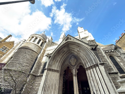 Konstfotografi Gothic Church Portals: The intimidating and ornate wooden doors of a Gothic church set against a clear blue sky with dramatic white clouds