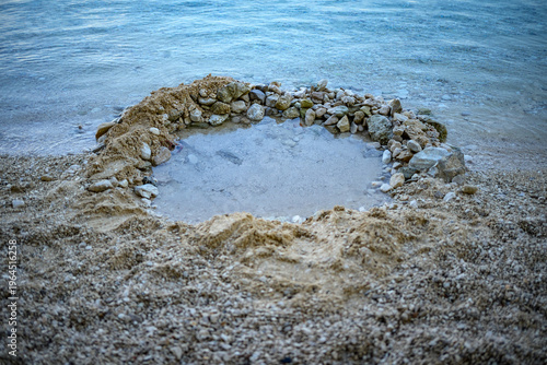 Foto Stone-lined sand pool on pebbly beach by calm sea