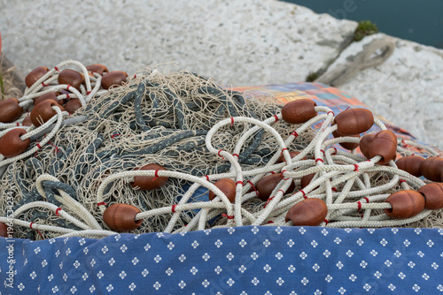 Professional fishing nets piled in plastic bins on the harbor dock in Grado, Italy. Close-up of traditional nautical gear, ropes and floats in the port, maritime industry and fishing tradition.